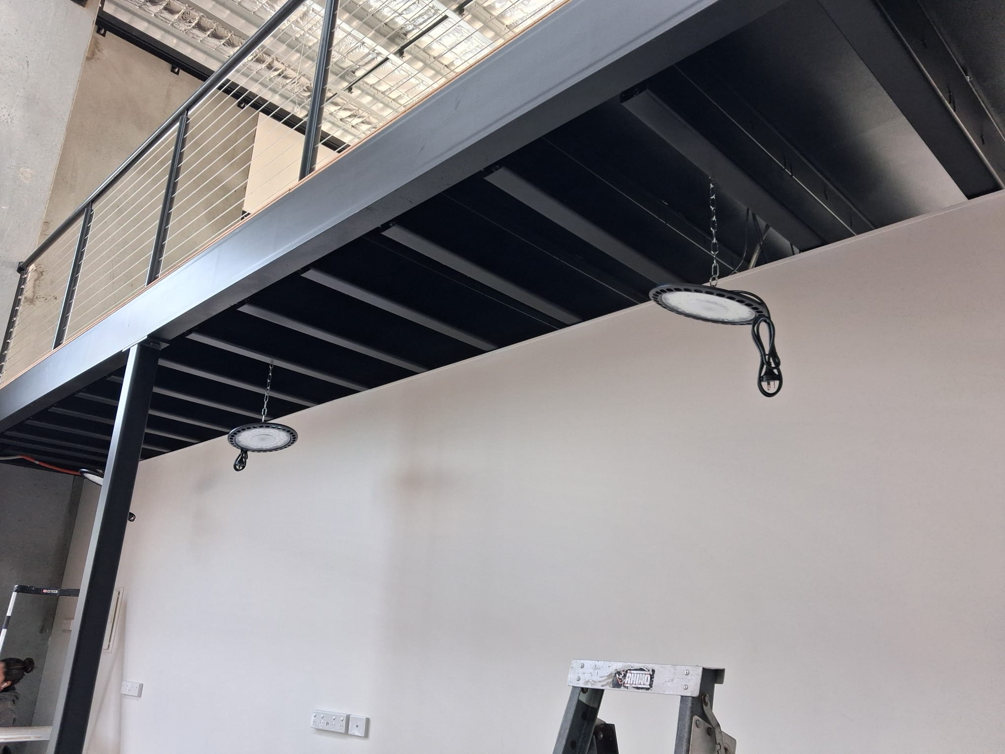 Steel mezzanine and high-bay lighting over the ground-floor workspace.